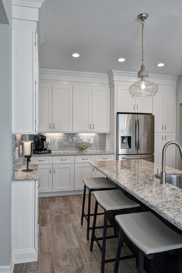 This is an example of a large contemporary l-shaped kitchen in Charleston with an undermount sink, shaker cabinets, white cabinets, granite benchtops, grey splashback, glass tile splashback, stainless steel appliances, porcelain floors, with island and brown floor.