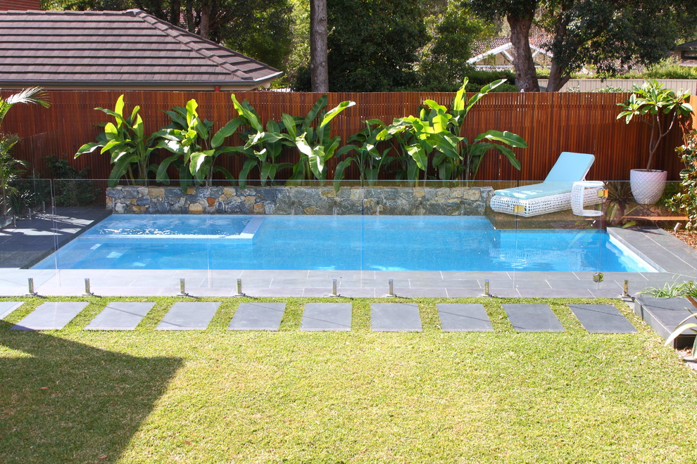 This is an example of a mid-sized tropical backyard rectangular lap pool in Sydney with natural stone pavers and a hot tub.