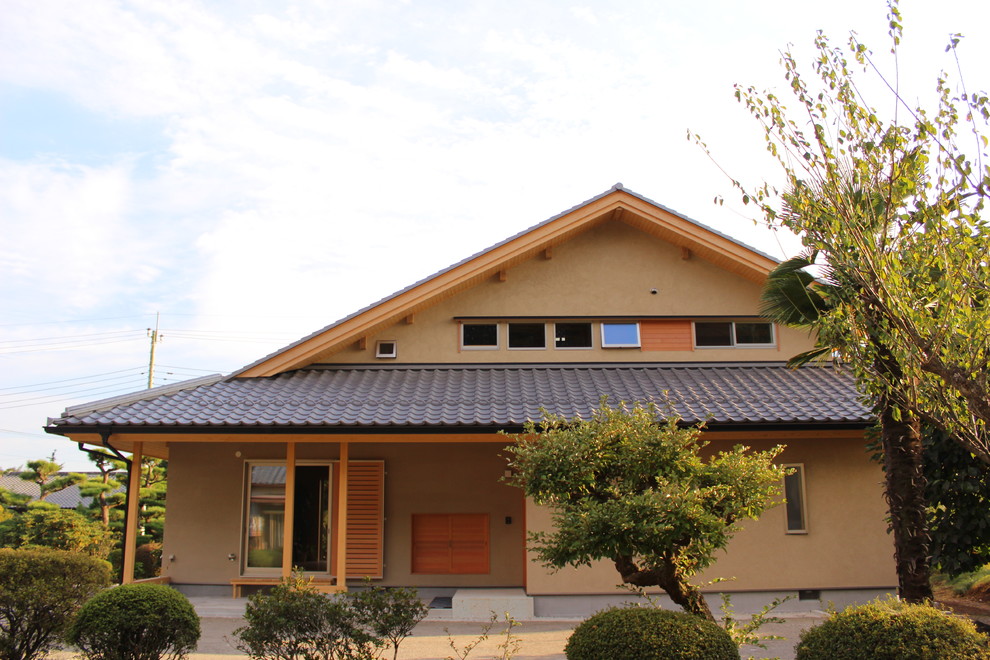This is an example of a mid-sized asian two-storey stucco house exterior in Other with a gable roof and a tile roof.