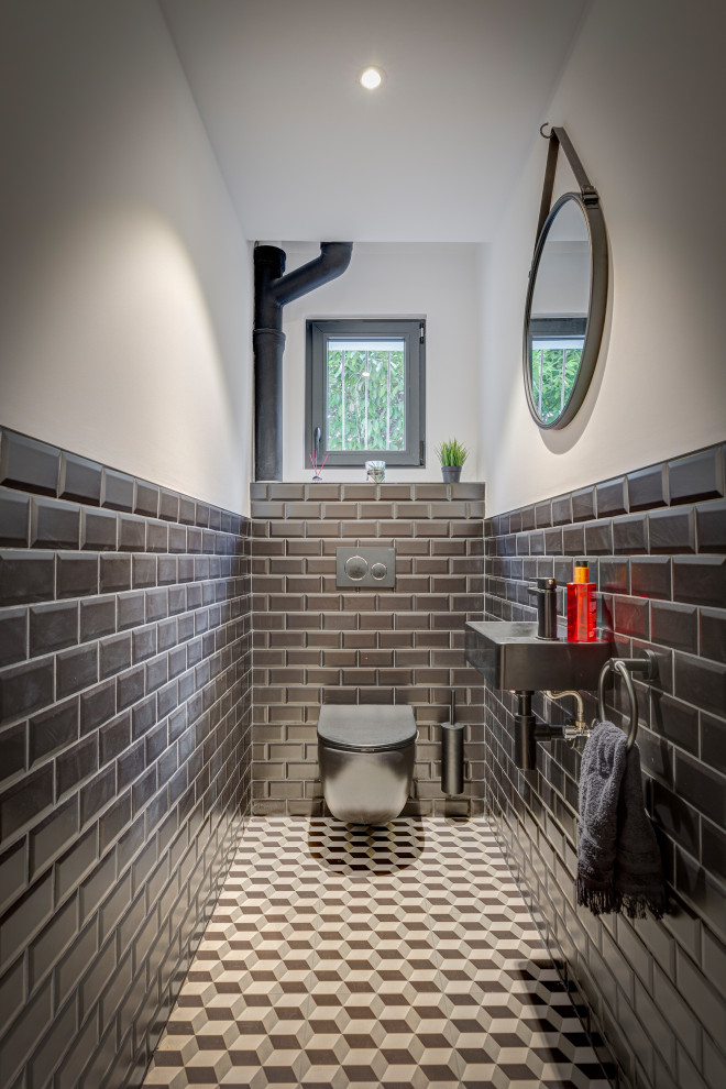 Idee per un bagno di servizio industriale di medie dimensioni con WC sospeso, piastrelle nere, piastrelle diamantate, pareti bianche, lavabo sospeso, pavimento multicolore e top nero