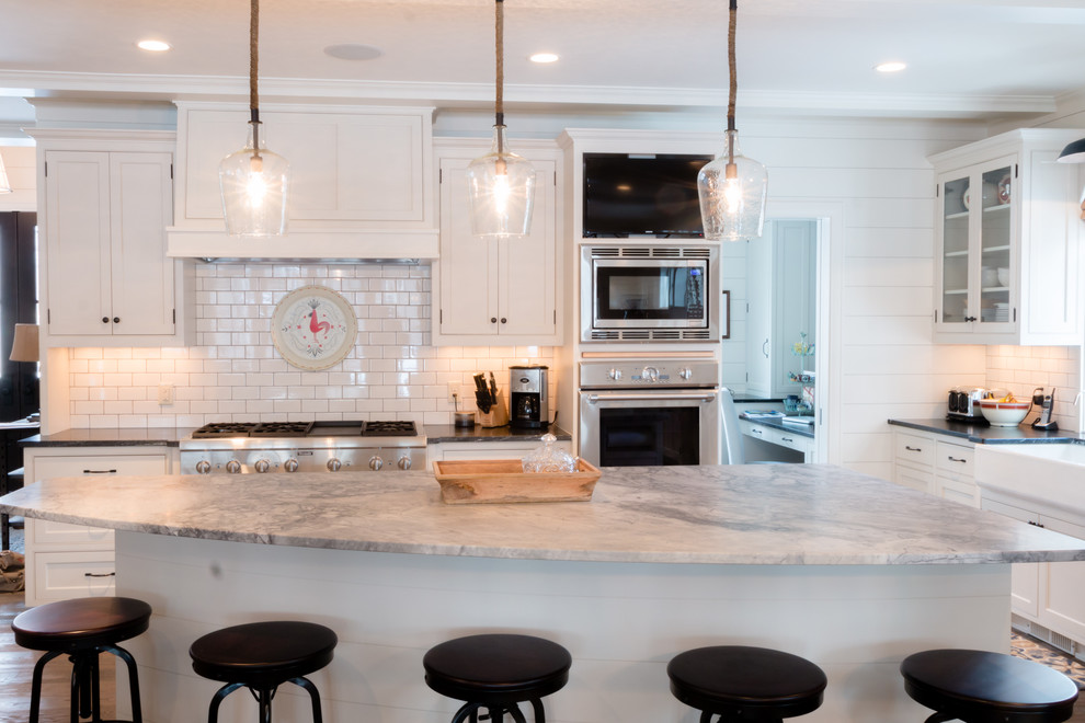 Inspiration for a large transitional l-shaped light wood floor open concept kitchen remodel in Minneapolis with a farmhouse sink, beaded inset cabinets, white cabinets, granite countertops, white backsplash, subway tile backsplash, stainless steel appliances and an island