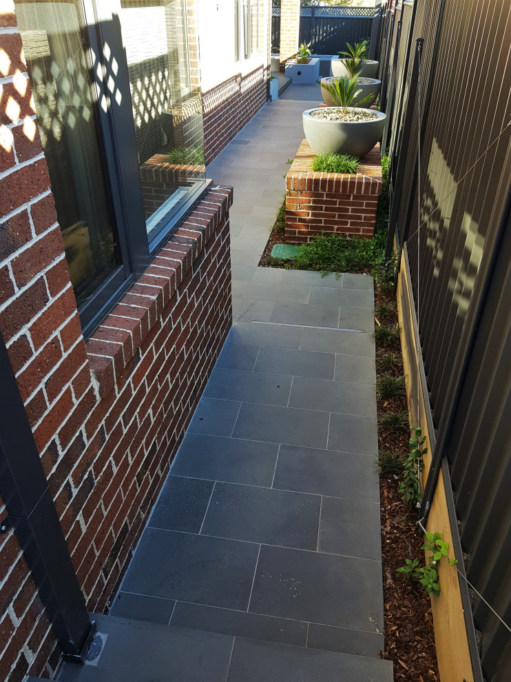 This is an example of a mid-sized modern backyard partial sun formal garden for summer in Melbourne with with flowerbed and natural stone pavers.
