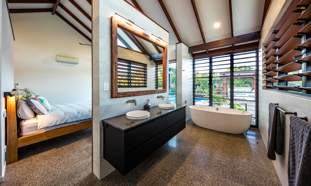 Tropical master bathroom in Cairns with flat-panel cabinets, black cabinets, a freestanding tub, gray tile, grey walls, concrete floors, a drop-in sink, grey floor and grey benchtops.