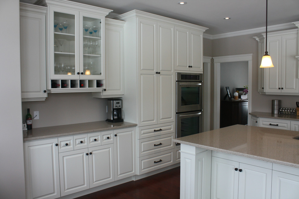 Example of a mid-sized transitional l-shaped medium tone wood floor eat-in kitchen design with an undermount sink, raised-panel cabinets, white cabinets, quartz countertops, stainless steel appliances and an island