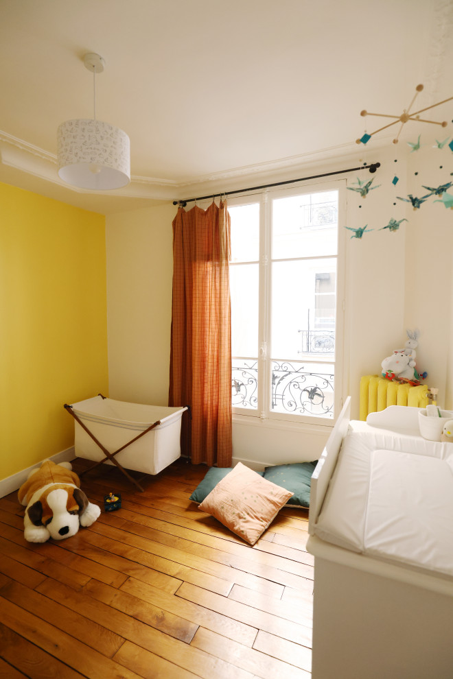 Esempio di una piccola cameretta per bambini da 1 a 3 anni boho chic con pareti gialle, pavimento in legno massello medio e pavimento marrone
