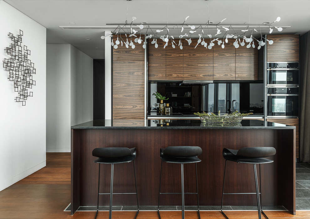 This is an example of a mid-sized contemporary single-wall open plan kitchen in Moscow with an undermount sink, flat-panel cabinets, medium wood cabinets, quartz benchtops, black splashback, glass sheet splashback, porcelain floors, with island, black floor and black appliances.