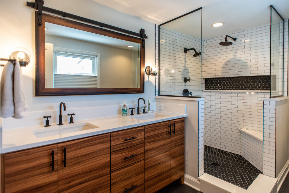 Inspiration for a mid-sized industrial master bathroom in Milwaukee with flat-panel cabinets, medium wood cabinets, a corner shower, white tile, porcelain tile, grey walls, porcelain floors, an undermount sink, black floor, an open shower, a shower seat, a double vanity and a built-in vanity.
