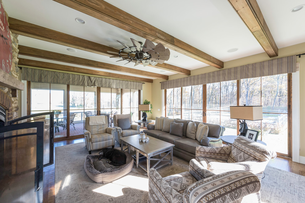 This is an example of a mid-sized country enclosed family room in New York with yellow walls, medium hardwood floors, a two-sided fireplace, a stone fireplace surround, a wall-mounted tv and brown floor.