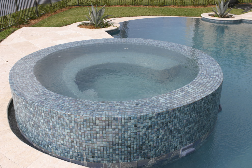 Photo of a mid-sized modern backyard round pool in Miami with a hot tub and natural stone pavers.