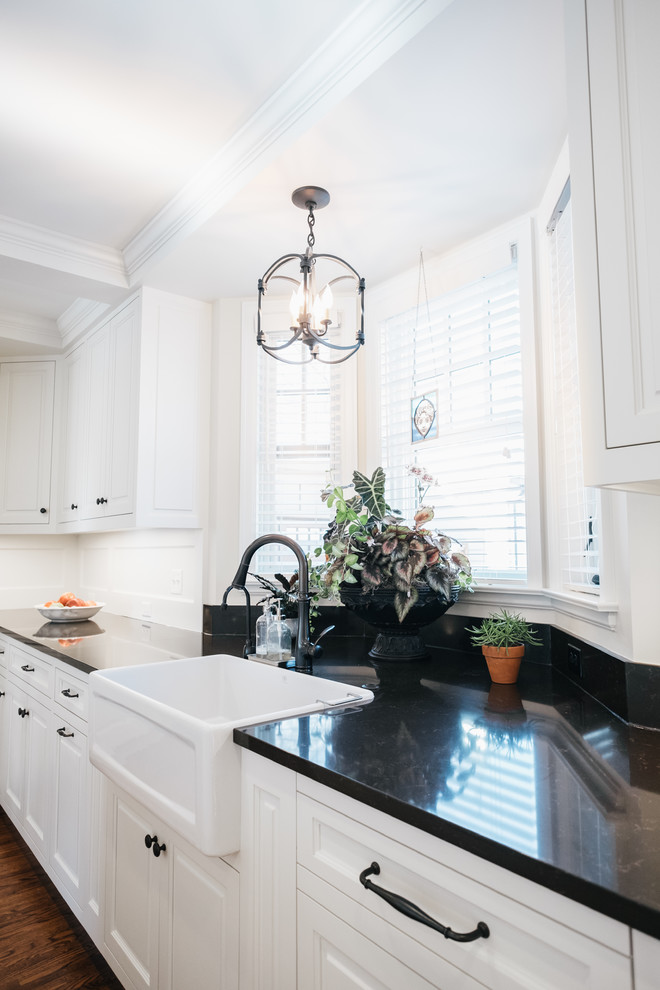 Mid-sized traditional l-shaped eat-in kitchen in Minneapolis with a farmhouse sink, raised-panel cabinets, white cabinets, onyx benchtops, panelled appliances, light hardwood floors and with island.