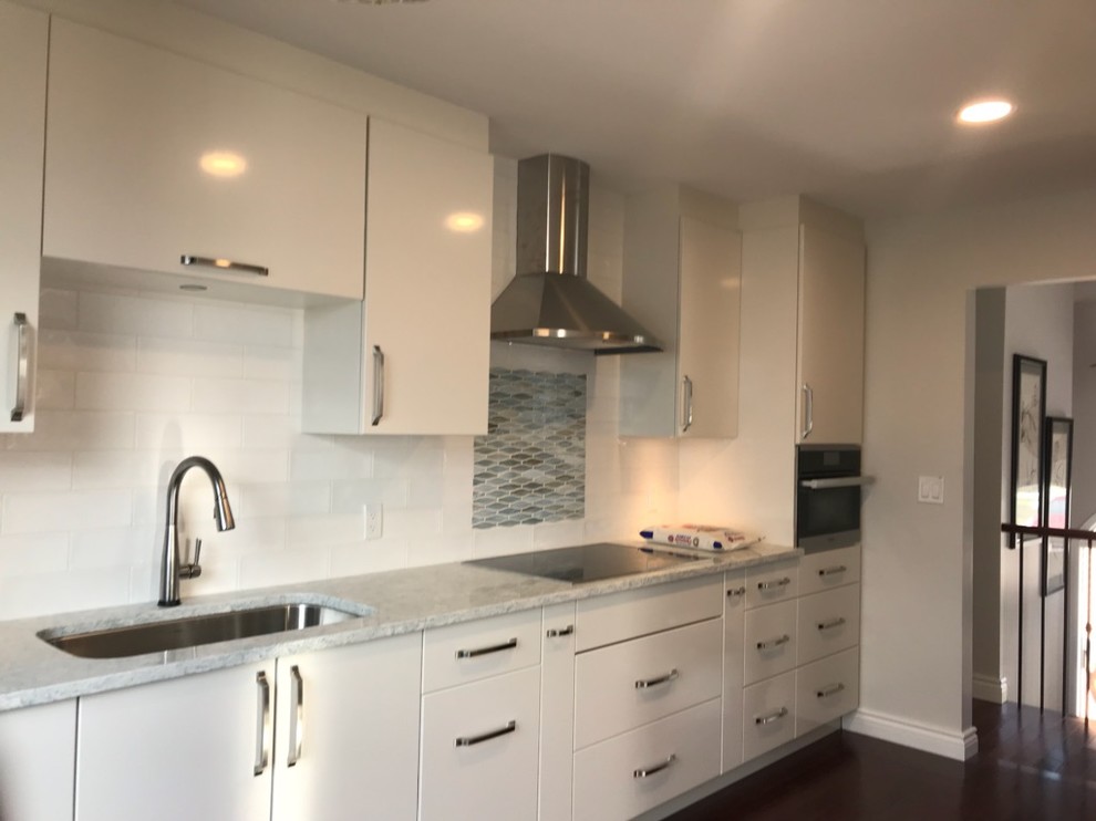 Example of a small galley dark wood floor enclosed kitchen design with an undermount sink, flat-panel cabinets, white cabinets, granite countertops, white backsplash, ceramic backsplash, stainless steel appliances, no island and gray countertops