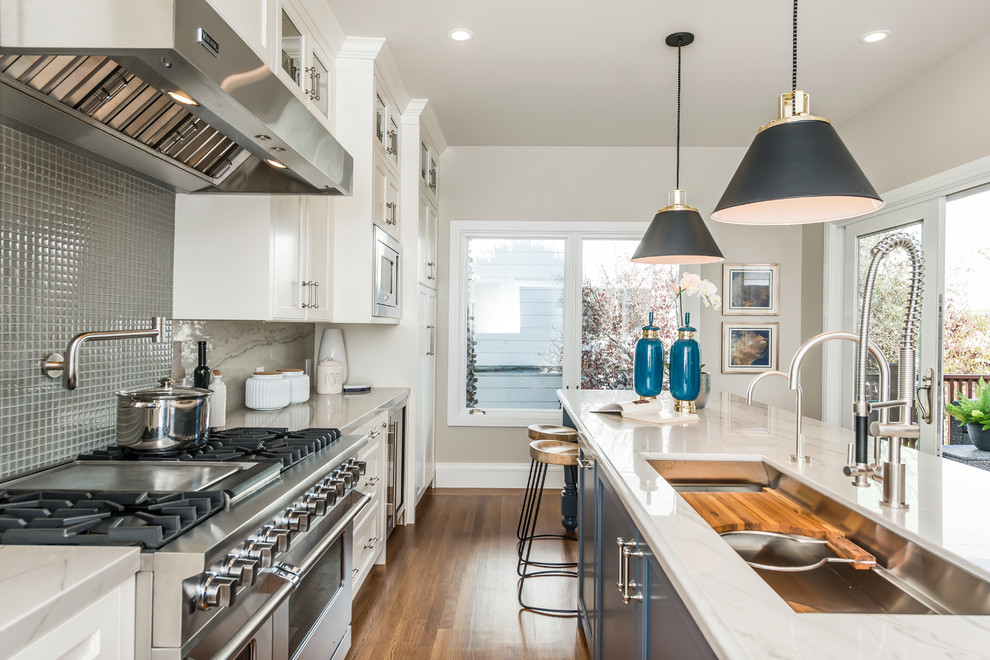 Transitional galley kitchen in San Francisco with an undermount sink, recessed-panel cabinets, white cabinets, grey splashback, mosaic tile splashback, stainless steel appliances, medium hardwood floors and with island.