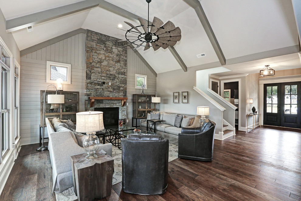 Photo of a large arts and crafts open concept family room in Other with grey walls, medium hardwood floors, a standard fireplace, a stone fireplace surround, a wall-mounted tv and brown floor.