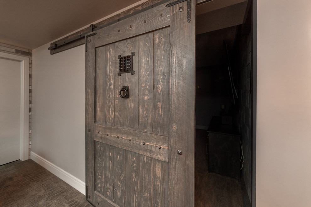 This is an example of a large country walk-out basement in Edmonton with a game room, grey walls, carpet, a standard fireplace, a brick fireplace surround, brown floor, exposed beam and panelled walls.