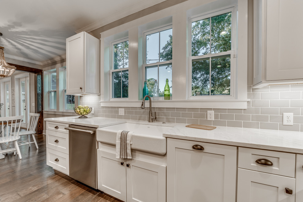 This is an example of a mid-sized country u-shaped open plan kitchen in Jacksonville with a farmhouse sink, shaker cabinets, white cabinets, quartz benchtops, grey splashback, terra-cotta splashback, stainless steel appliances, with island, white benchtop, medium hardwood floors and brown floor.