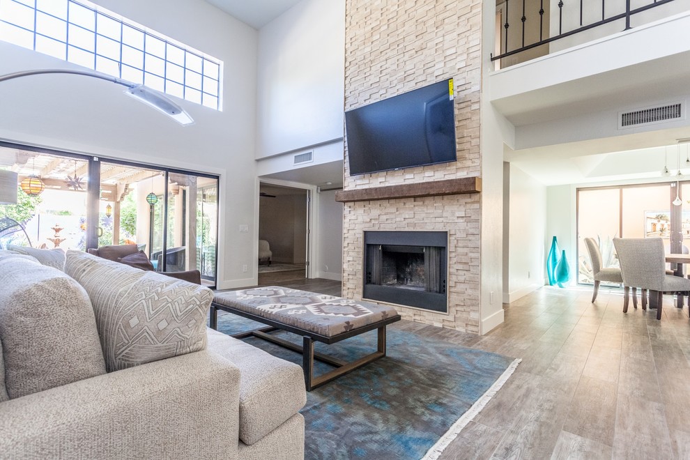 Design ideas for a large transitional open concept family room in Phoenix with beige walls, porcelain floors, a standard fireplace, a stone fireplace surround, a wall-mounted tv and brown floor.