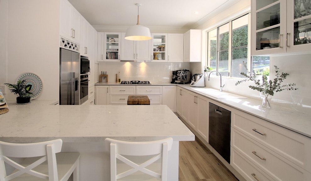 Photo of a traditional u-shaped eat-in kitchen in Sunshine Coast with a double-bowl sink, shaker cabinets, white cabinets, with island and white benchtop.