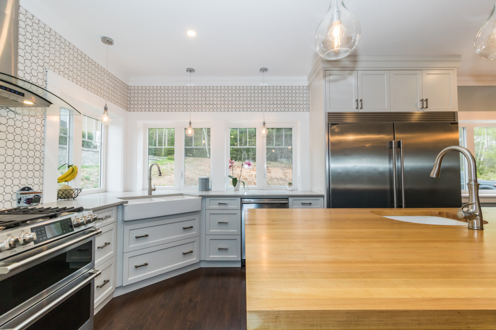 Mid-sized l-shaped vinyl floor and brown floor kitchen photo with a farmhouse sink, recessed-panel cabinets, white cabinets, multicolored backsplash, ceramic backsplash, stainless steel appliances, an island, gray countertops and quartzite countertops