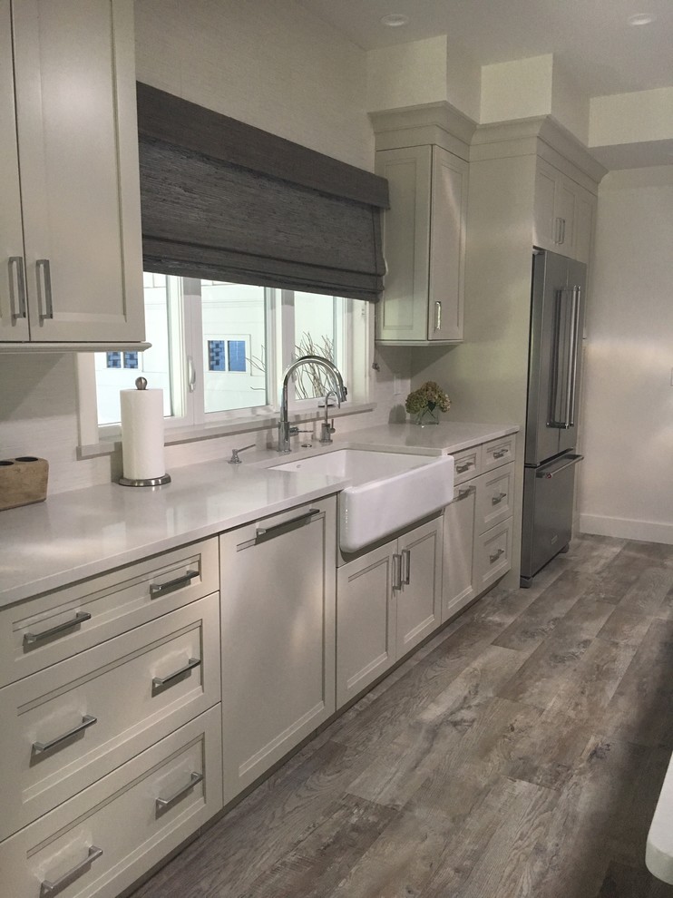 This is an example of a large transitional galley eat-in kitchen in Denver with a farmhouse sink, shaker cabinets, grey cabinets, stainless steel appliances, medium hardwood floors, with island, brown floor, solid surface benchtops and white splashback.
