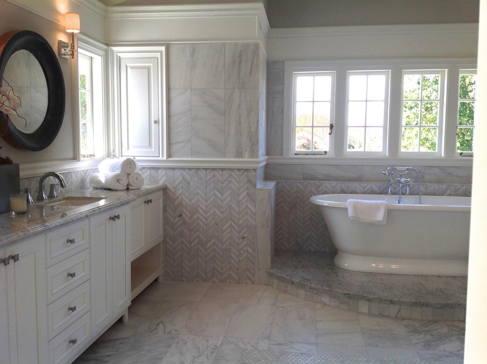 This is an example of a large transitional master bathroom in Los Angeles with recessed-panel cabinets, white cabinets, a freestanding tub, a corner shower, a one-piece toilet, gray tile, marble, white walls, marble floors, marble benchtops, a sliding shower screen and white benchtops.