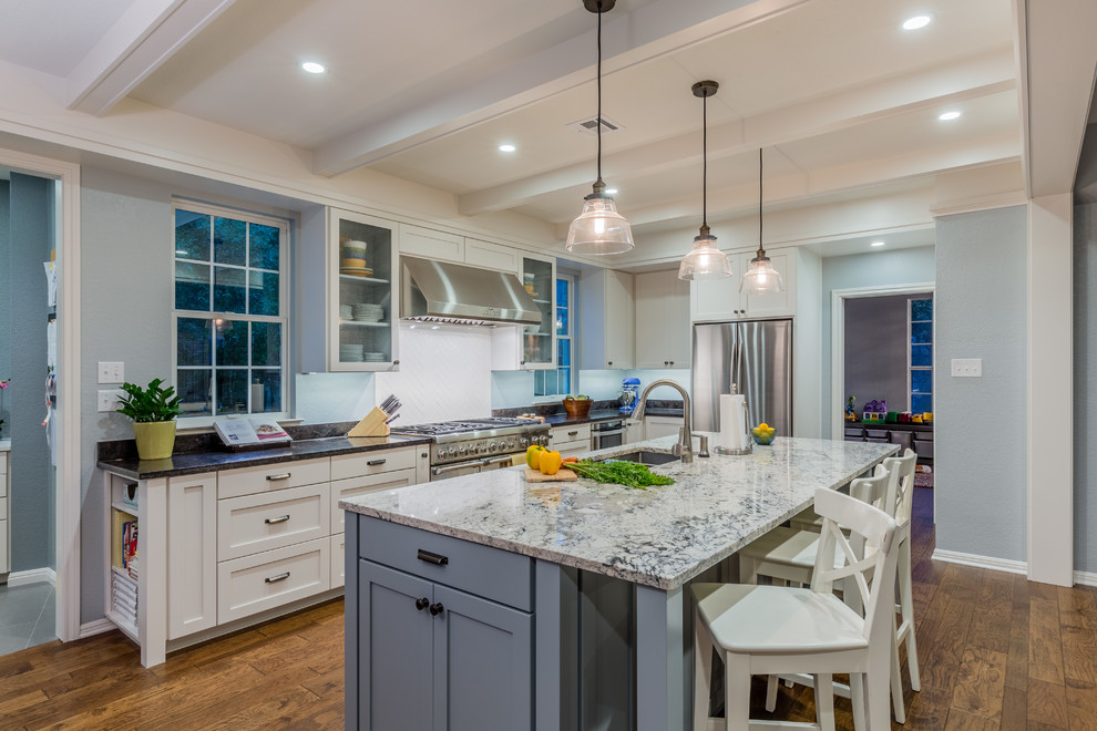 Open concept kitchen - large transitional l-shaped medium tone wood floor open concept kitchen idea in Austin with a double-bowl sink, recessed-panel cabinets, gray cabinets, granite countertops, white backsplash, ceramic backsplash, stainless steel appliances and an island
