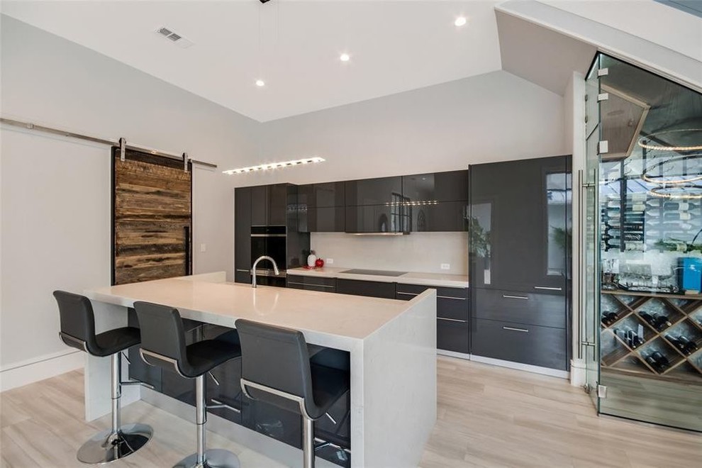 Inspiration for a mid-sized contemporary single-wall open plan kitchen in Houston with an undermount sink, flat-panel cabinets, grey cabinets, solid surface benchtops, beige splashback, stone slab splashback, stainless steel appliances, light hardwood floors, with island, brown floor and beige benchtop.