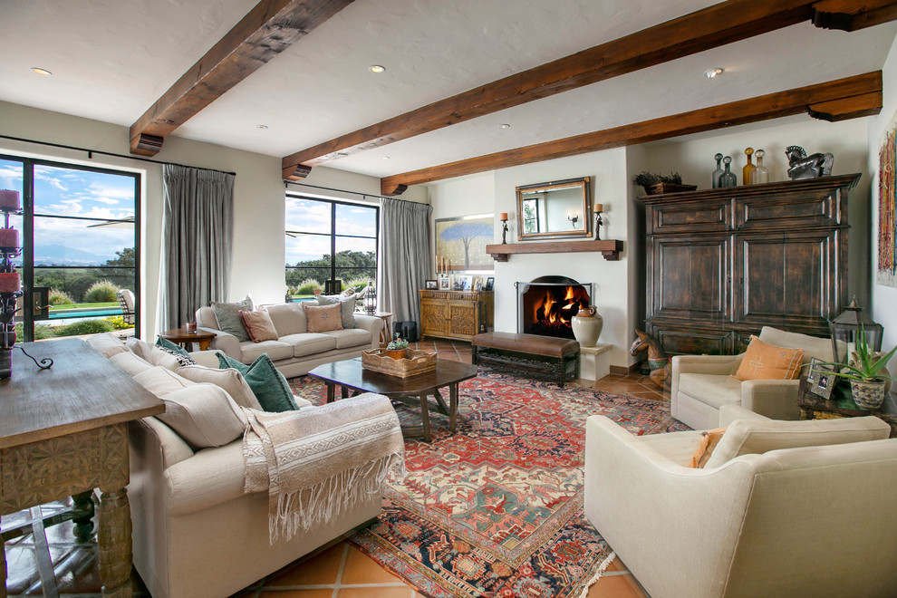 Design ideas for a large mediterranean living room in San Luis Obispo with white walls, terra-cotta floors, a standard fireplace, a plaster fireplace surround and brown floor.