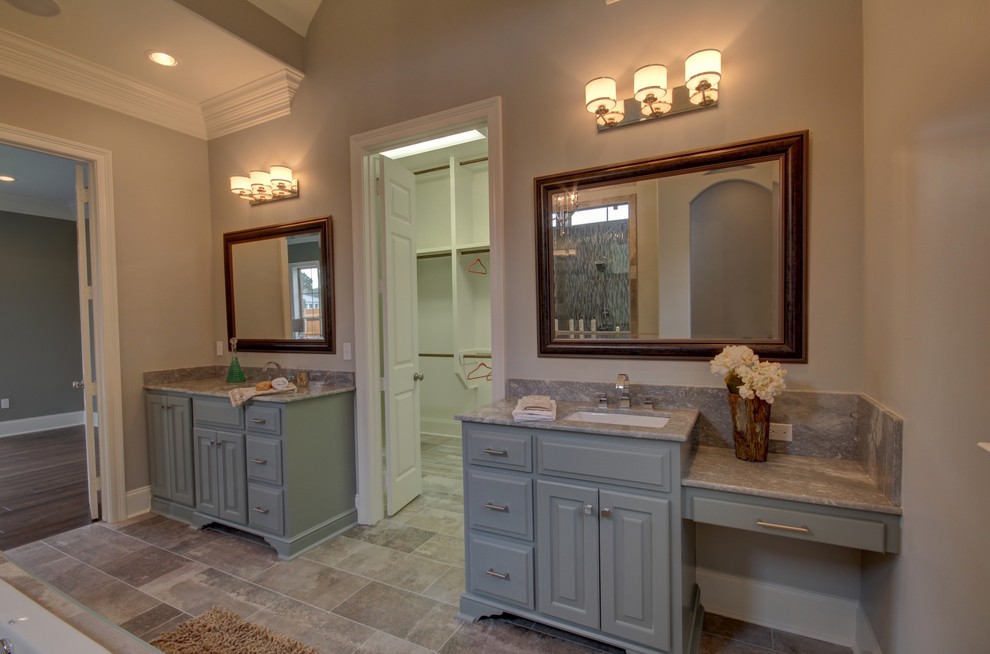 This is an example of a transitional bathroom in New Orleans with grey cabinets, a drop-in tub, a one-piece toilet, gray tile, an undermount sink and granite benchtops.