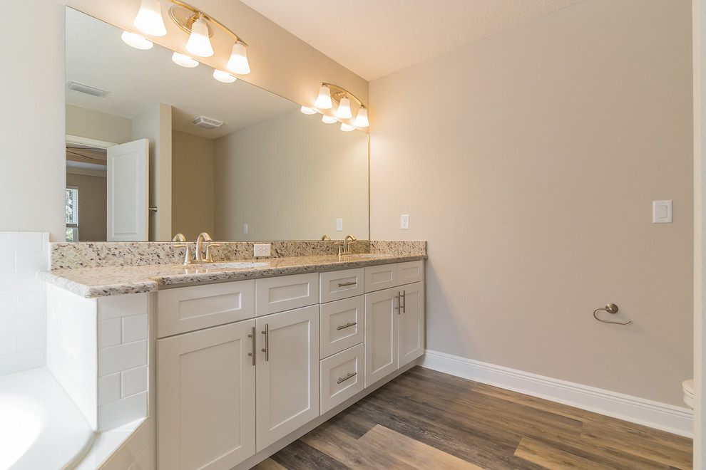 Mid-sized transitional master bathroom in Orlando with shaker cabinets, white cabinets, white tile, ceramic tile, laminate floors, granite benchtops, grey floor, a hinged shower door, a hot tub and a corner shower.