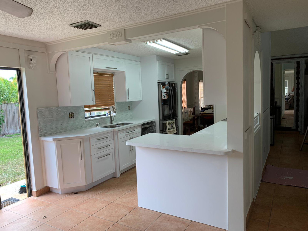 Mid-sized transitional galley separate kitchen in Miami with a double-bowl sink, shaker cabinets, white cabinets, quartz benchtops, white splashback, matchstick tile splashback, black appliances, porcelain floors, no island, beige floor and white benchtop.
