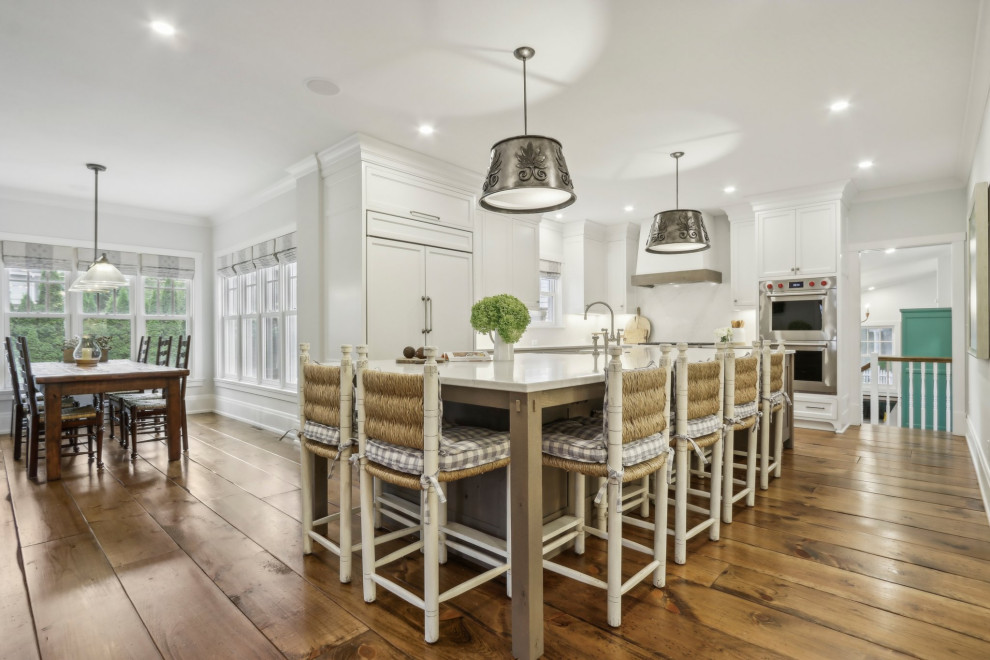 Eat-in kitchen - mid-sized rustic l-shaped medium tone wood floor and brown floor eat-in kitchen idea in Milwaukee with a farmhouse sink, shaker cabinets, white cabinets, quartz countertops, white backsplash, quartz backsplash, stainless steel appliances, an island and multicolored countertops
