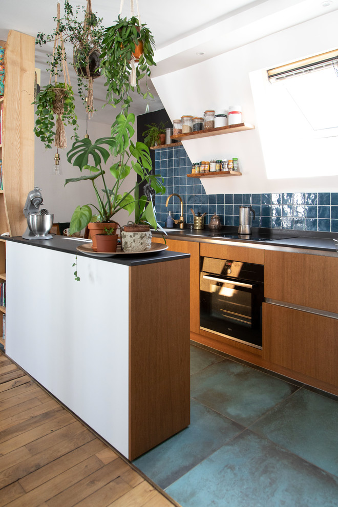 Photo of a small eclectic galley open plan kitchen in Other with flat-panel cabinets, blue splashback, ceramic splashback, black appliances, ceramic floors, blue floor, black benchtop, medium wood cabinets, a peninsula, an undermount sink and solid surface benchtops.