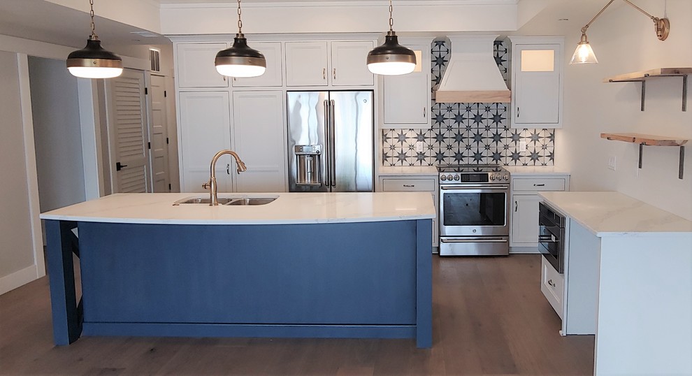 Open concept kitchen - mid-sized eclectic l-shaped medium tone wood floor and brown floor open concept kitchen idea with a double-bowl sink, recessed-panel cabinets, white cabinets, quartzite countertops, gray backsplash, mosaic tile backsplash, stainless steel appliances, an island and white countertops