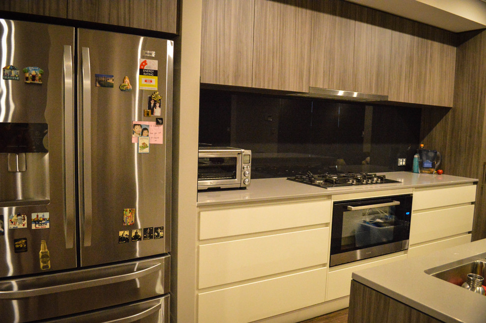 Midcentury galley eat-in kitchen in Perth with a double-bowl sink, medium wood cabinets, solid surface benchtops, black splashback, glass sheet splashback, stainless steel appliances, vinyl floors and with island.
