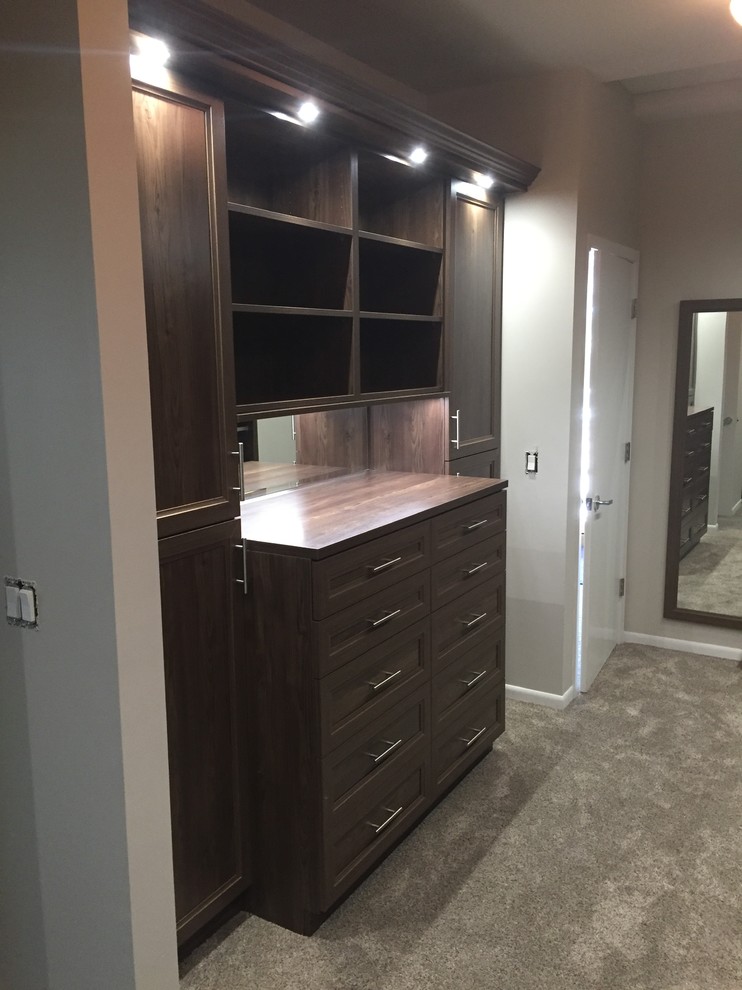 Design ideas for a mid-sized traditional gender-neutral walk-in wardrobe in Minneapolis with recessed-panel cabinets, dark wood cabinets and carpet.