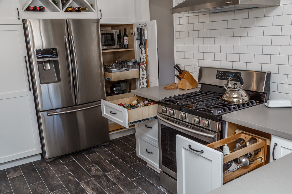 This is an example of a mid-sized contemporary u-shaped separate kitchen in Orange County with a farmhouse sink, shaker cabinets, white cabinets, concrete benchtops, white splashback, subway tile splashback, stainless steel appliances, laminate floors, a peninsula, black floor and grey benchtop.