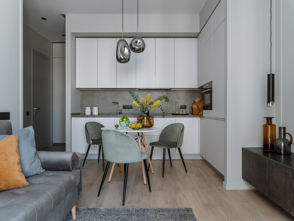 Photo of a contemporary l-shaped open plan kitchen in Moscow with flat-panel cabinets, white cabinets, grey splashback, stainless steel appliances, light hardwood floors, no island, beige floor and grey benchtop.