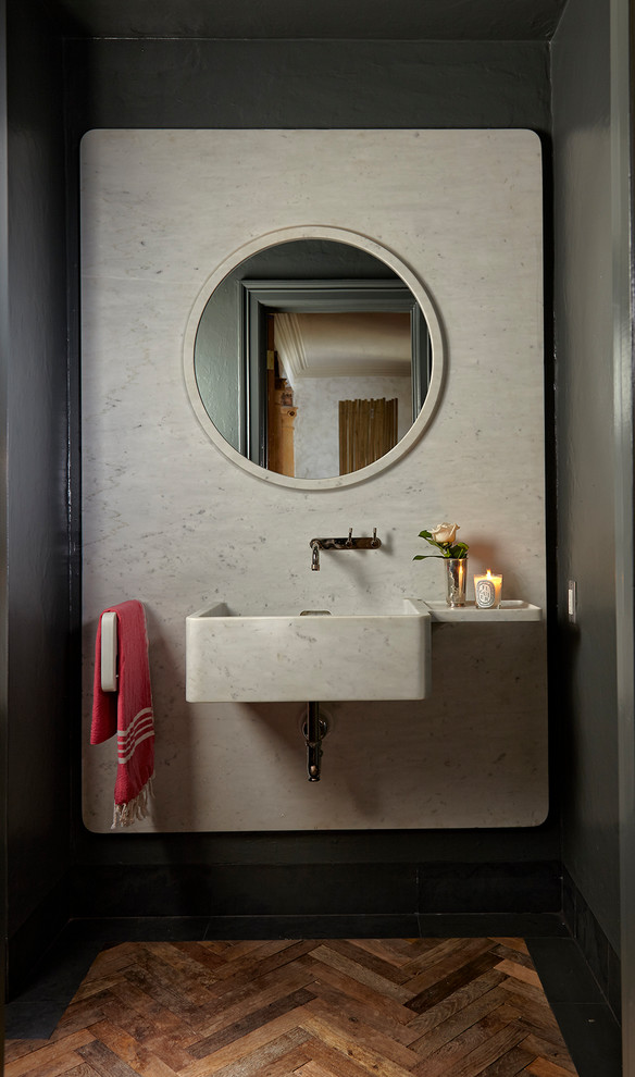 This is an example of a mediterranean powder room in Miami with white tile, grey walls, medium hardwood floors, a wall-mount sink, brown floor and white benchtops.