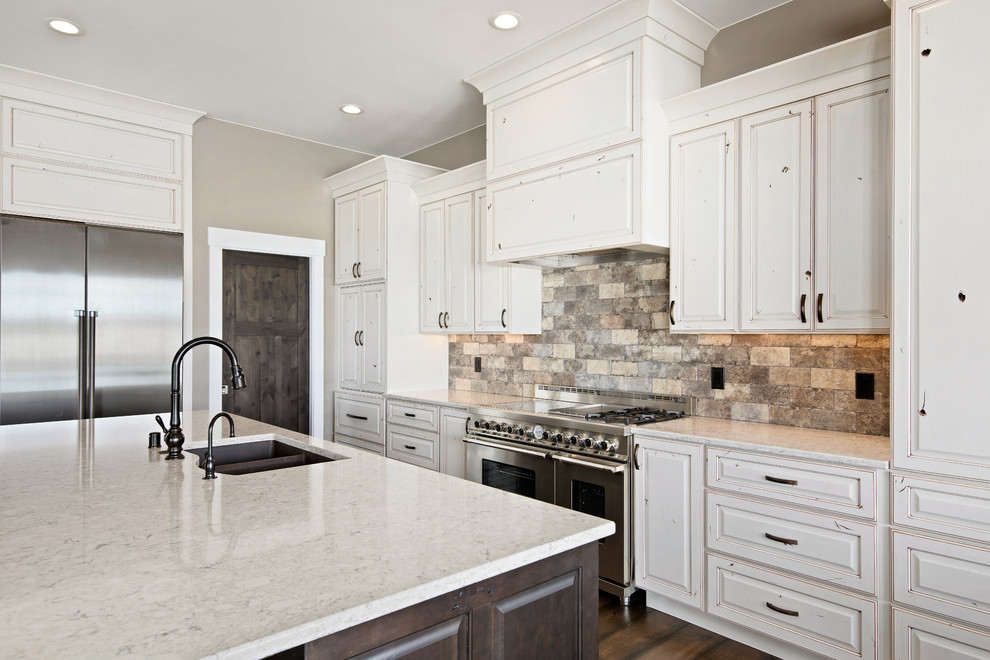 Large transitional l-shaped medium tone wood floor and brown floor eat-in kitchen photo with an undermount sink, raised-panel cabinets, quartz countertops, beige backsplash, stone tile backsplash, stainless steel appliances, an island and beige countertops