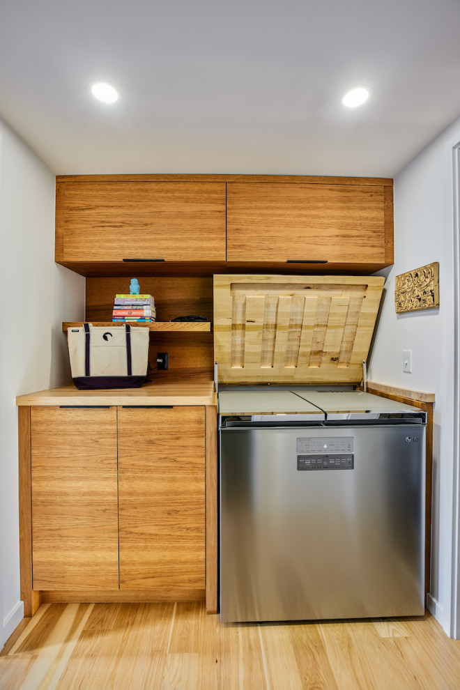 Inspiration for a mid-sized midcentury galley utility room in Detroit with a drop-in sink, flat-panel cabinets, medium wood cabinets, wood benchtops, beige splashback, timber splashback, white walls, medium hardwood floors, a stacked washer and dryer, beige floor and beige benchtop.