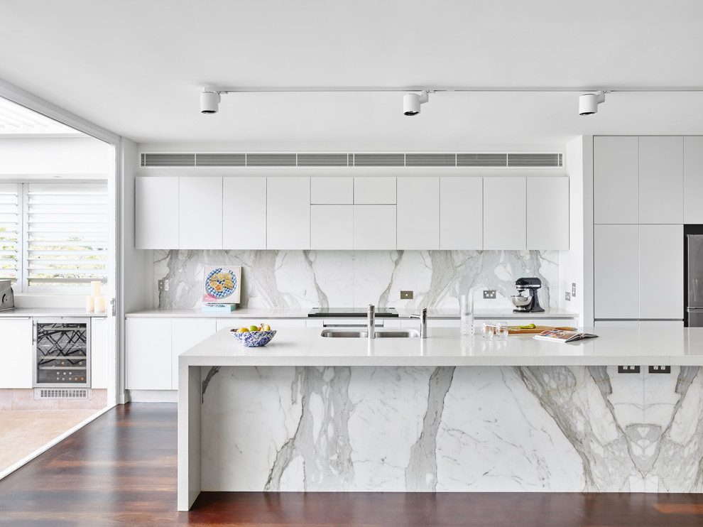 Inspiration for a contemporary galley kitchen in Brisbane with an undermount sink, flat-panel cabinets, white cabinets, grey splashback, stone slab splashback, stainless steel appliances, dark hardwood floors, with island and brown floor.