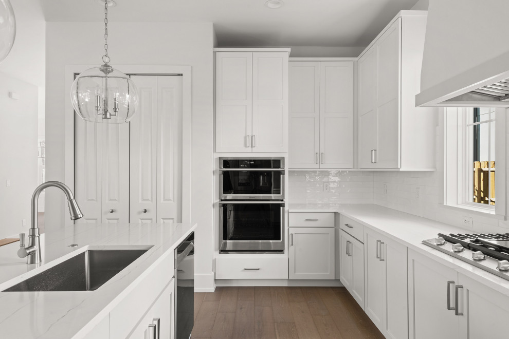 Inspiration for a large transitional u-shaped medium tone wood floor and brown floor eat-in kitchen remodel in Orlando with an undermount sink, shaker cabinets, white cabinets, marble countertops, white backsplash, porcelain backsplash, stainless steel appliances, an island and white countertops