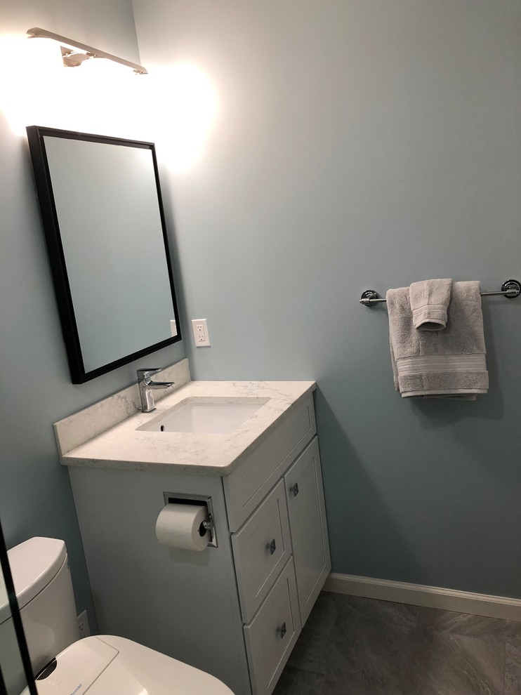 Photo of a small transitional bathroom in Burlington with raised-panel cabinets, grey cabinets, an alcove tub, a shower/bathtub combo, a bidet, gray tile, porcelain tile, blue walls, porcelain floors, an undermount sink, engineered quartz benchtops, grey floor, a sliding shower screen and white benchtops.
