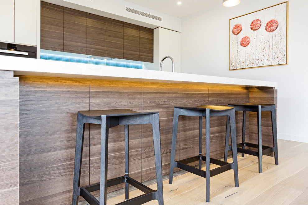 Photo of a mid-sized contemporary single-wall eat-in kitchen in Melbourne with a double-bowl sink, flat-panel cabinets, white cabinets, quartz benchtops, blue splashback, ceramic splashback, black appliances, light hardwood floors, with island and beige floor.