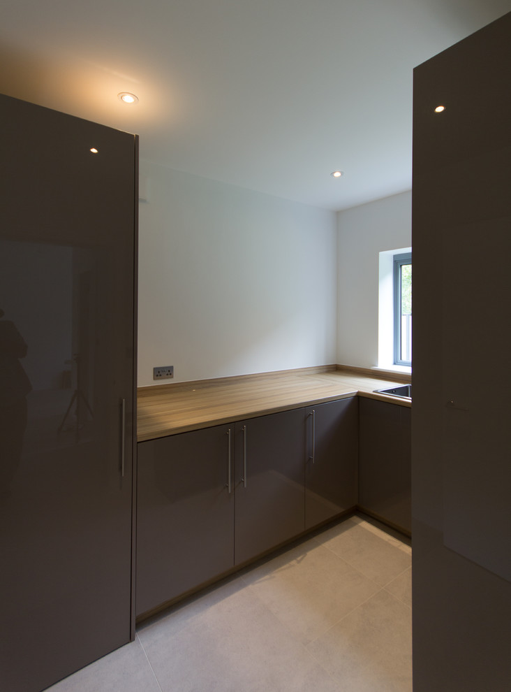 Photo of a medium sized modern u-shaped separated utility room in London with an integrated sink, flat-panel cabinets, brown cabinets, laminate countertops, white walls, porcelain flooring, a stacked washer and dryer and beige floors.