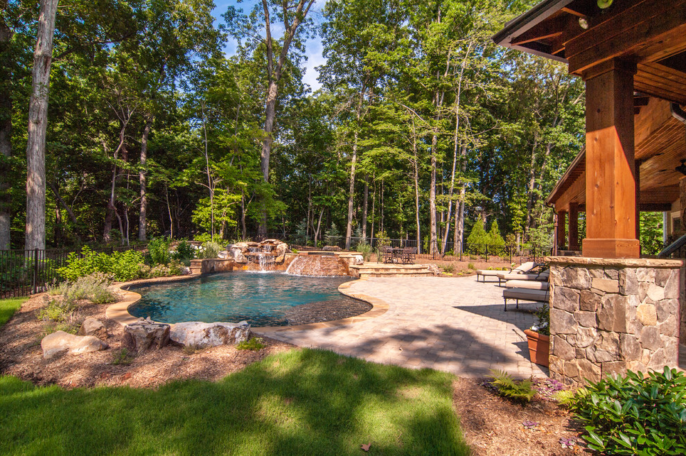Photo of a large arts and crafts backyard custom-shaped pool in Charlotte with a hot tub and natural stone pavers.