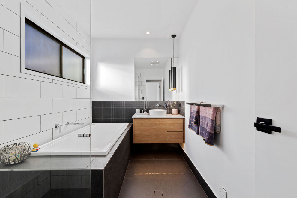 Inspiration for a contemporary bathroom in Sunshine Coast with flat-panel cabinets, medium wood cabinets, a drop-in tub, black and white tile, white walls, a vessel sink, grey floor and white benchtops.