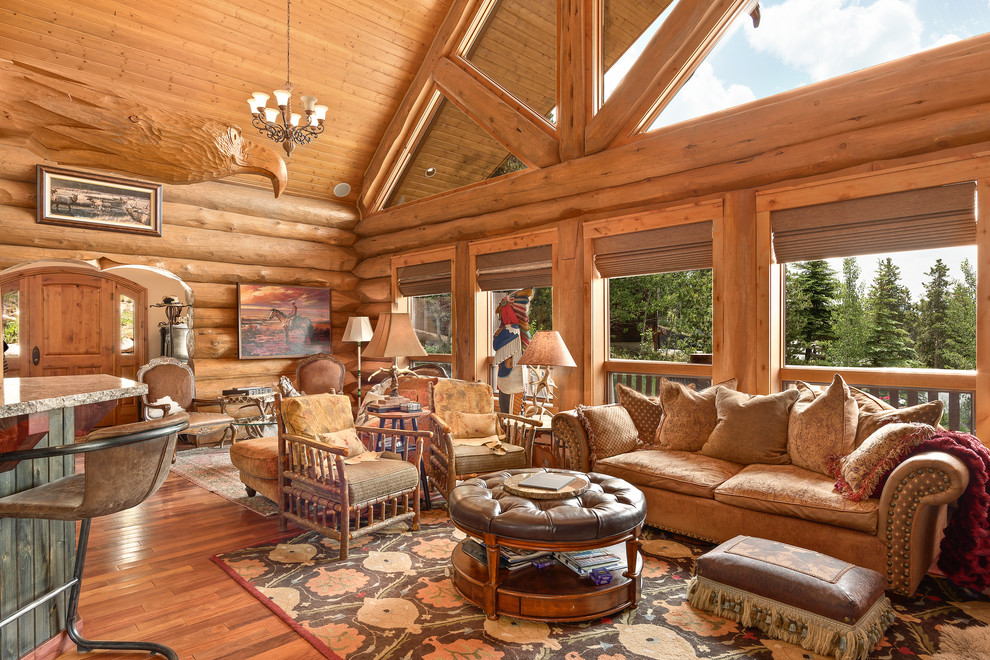 Inspiration for a large country open concept living room in Denver with medium hardwood floors, brown walls, a standard fireplace, a stone fireplace surround, a freestanding tv and brown floor.