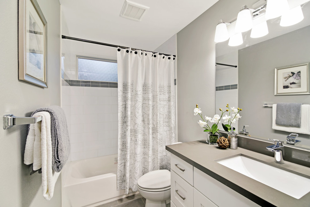 Photo of a mid-sized transitional kids bathroom in Seattle with shaker cabinets, white cabinets, an alcove tub, a shower/bathtub combo, a two-piece toilet, white tile, ceramic tile, grey walls, porcelain floors, an undermount sink, engineered quartz benchtops, grey floor, a shower curtain and grey benchtops.