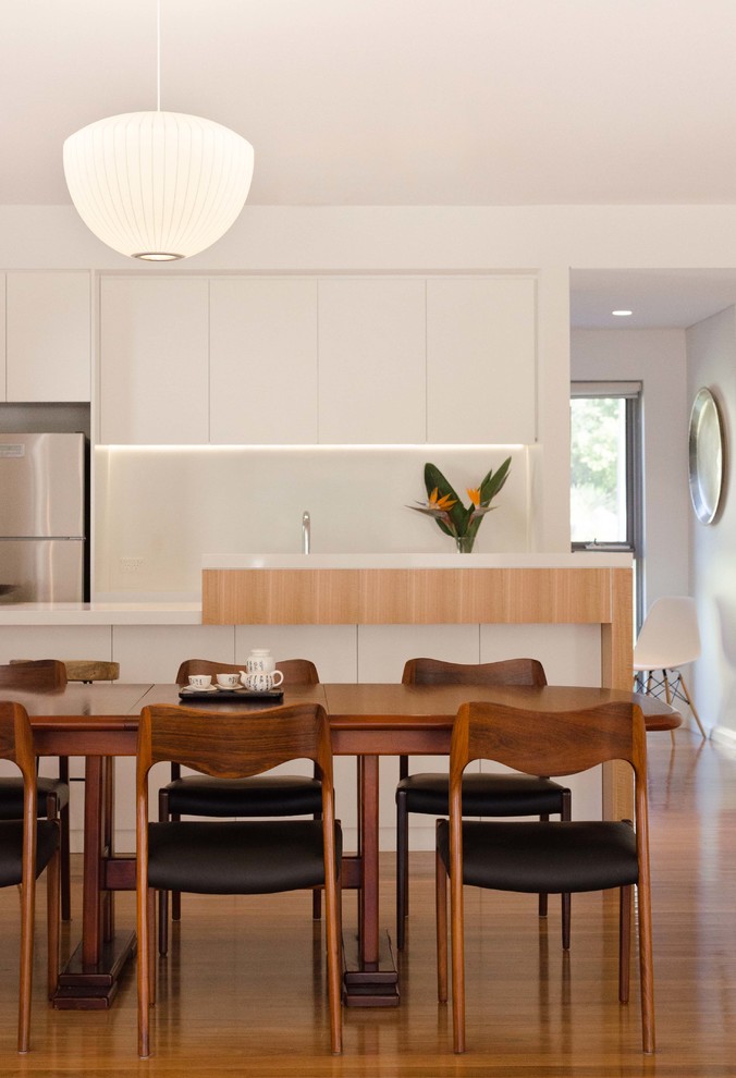 This is an example of a contemporary kitchen/dining combo in Sydney with white walls, medium hardwood floors and brown floor.